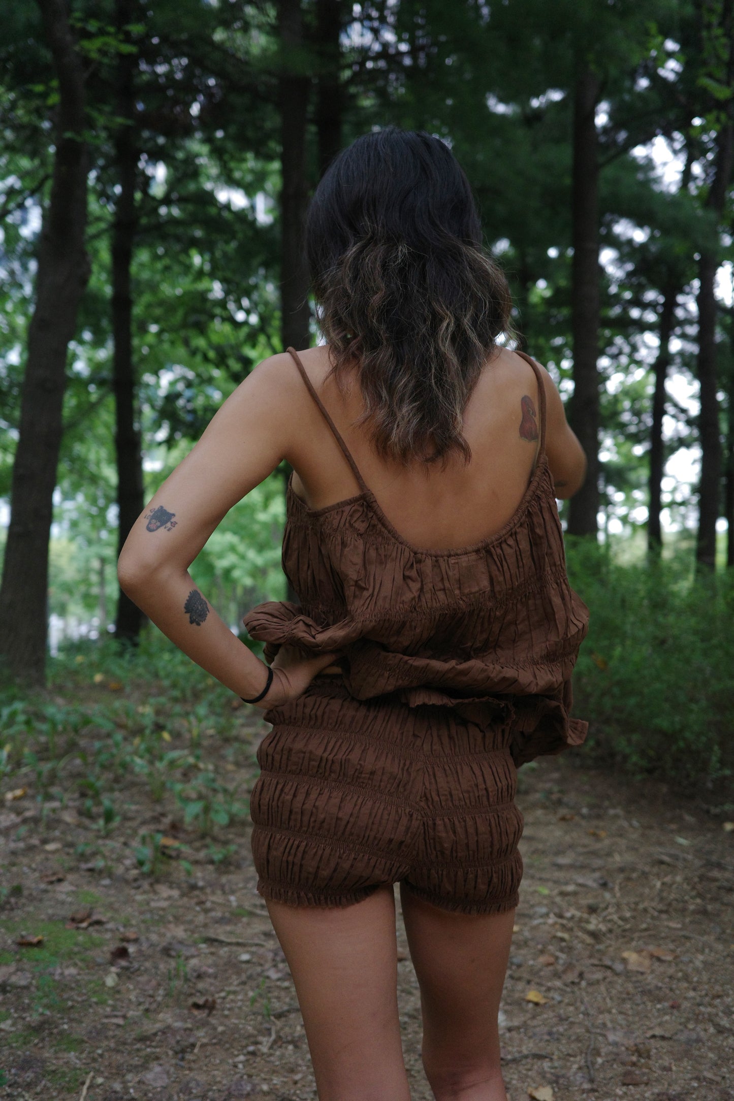 woman wearing a brown ruffle top and shorts in a forest setting