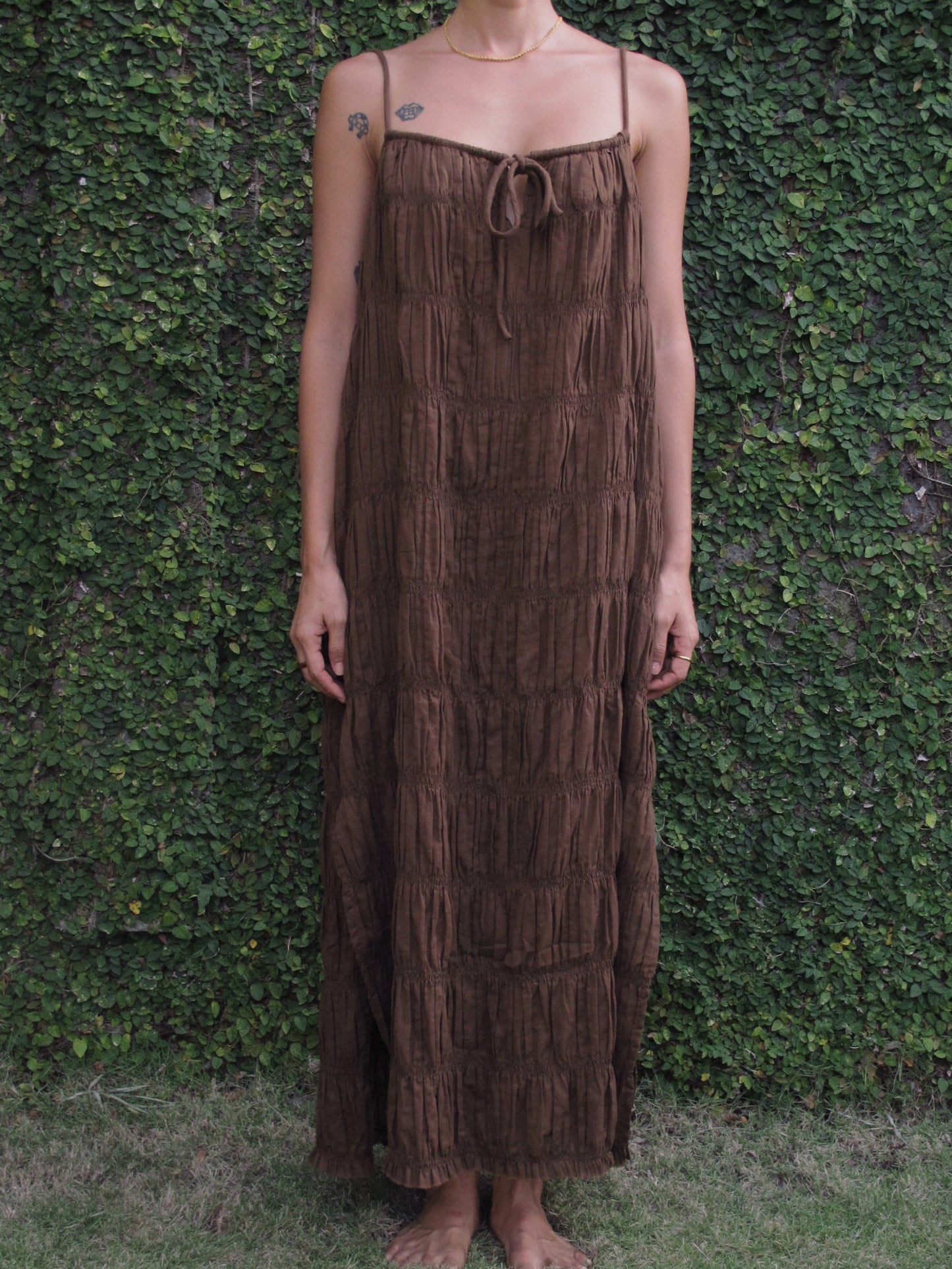 Person wearing a brown fringe dress standing against a green leafy background