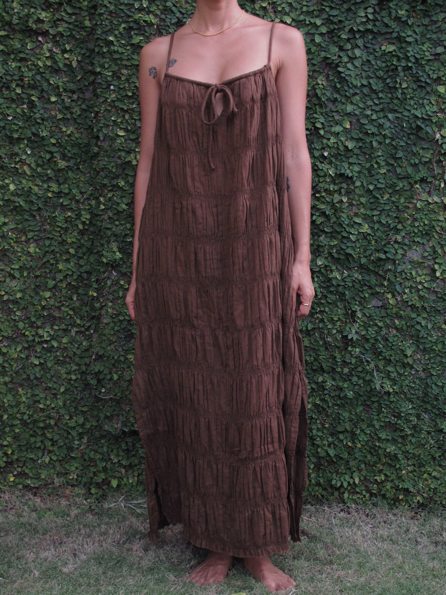 Person wearing a brown tiered dress against a green leafy background