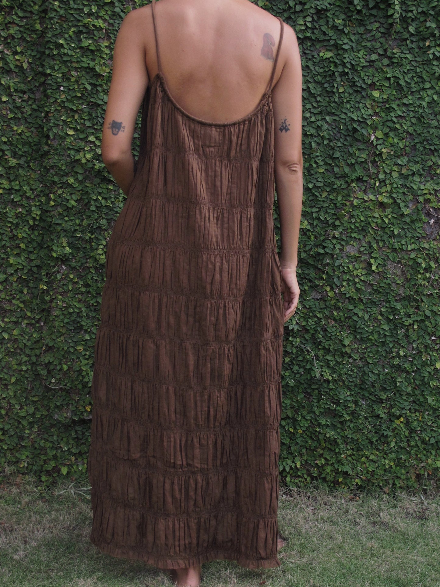 Person wearing a brown dress with a textured pattern against a green hedge background