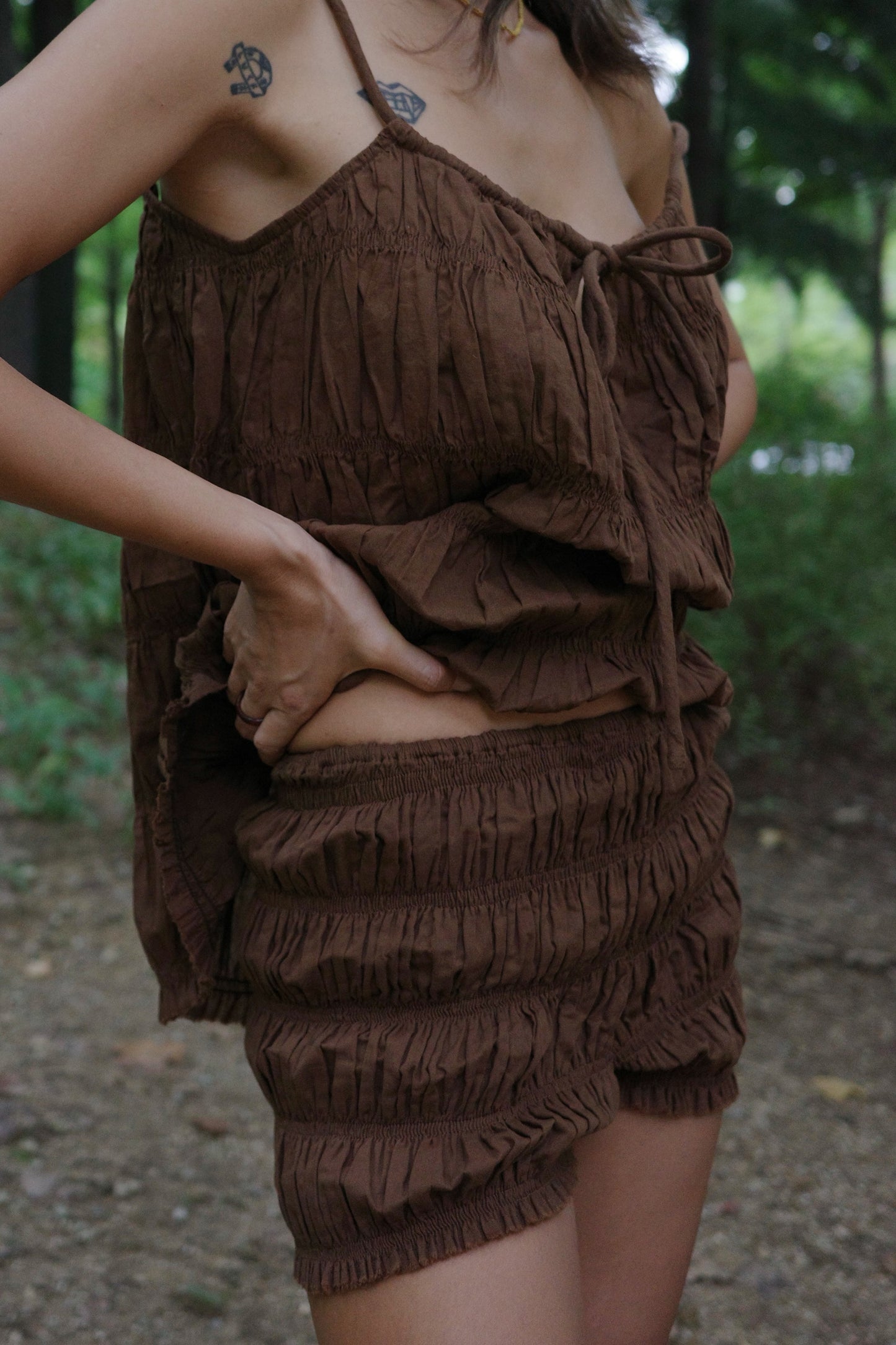 Brown ruffled shorts and string top worn by woman in a forest setting