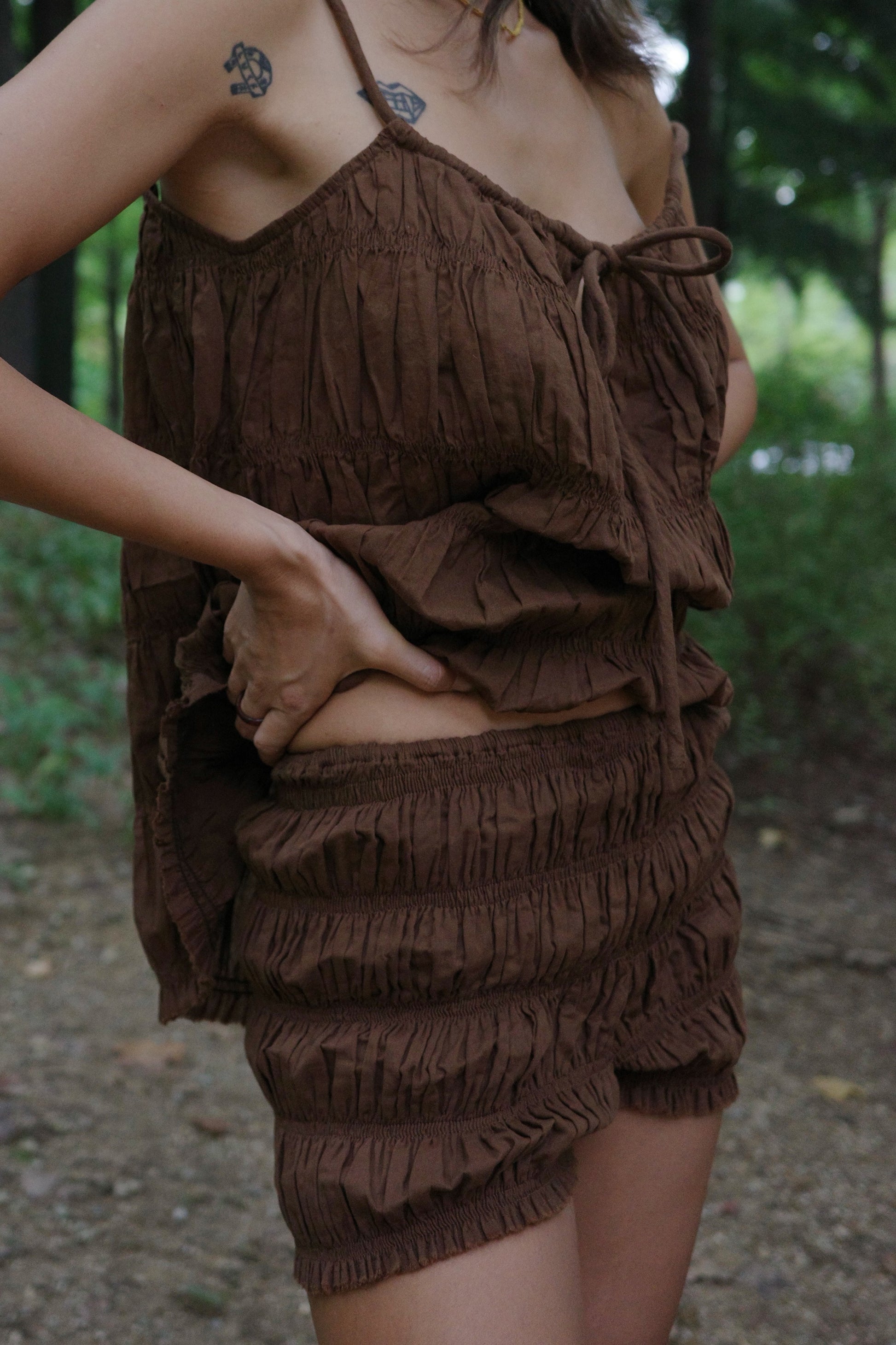 Brown ruffled shorts and string top worn by woman in a forest setting