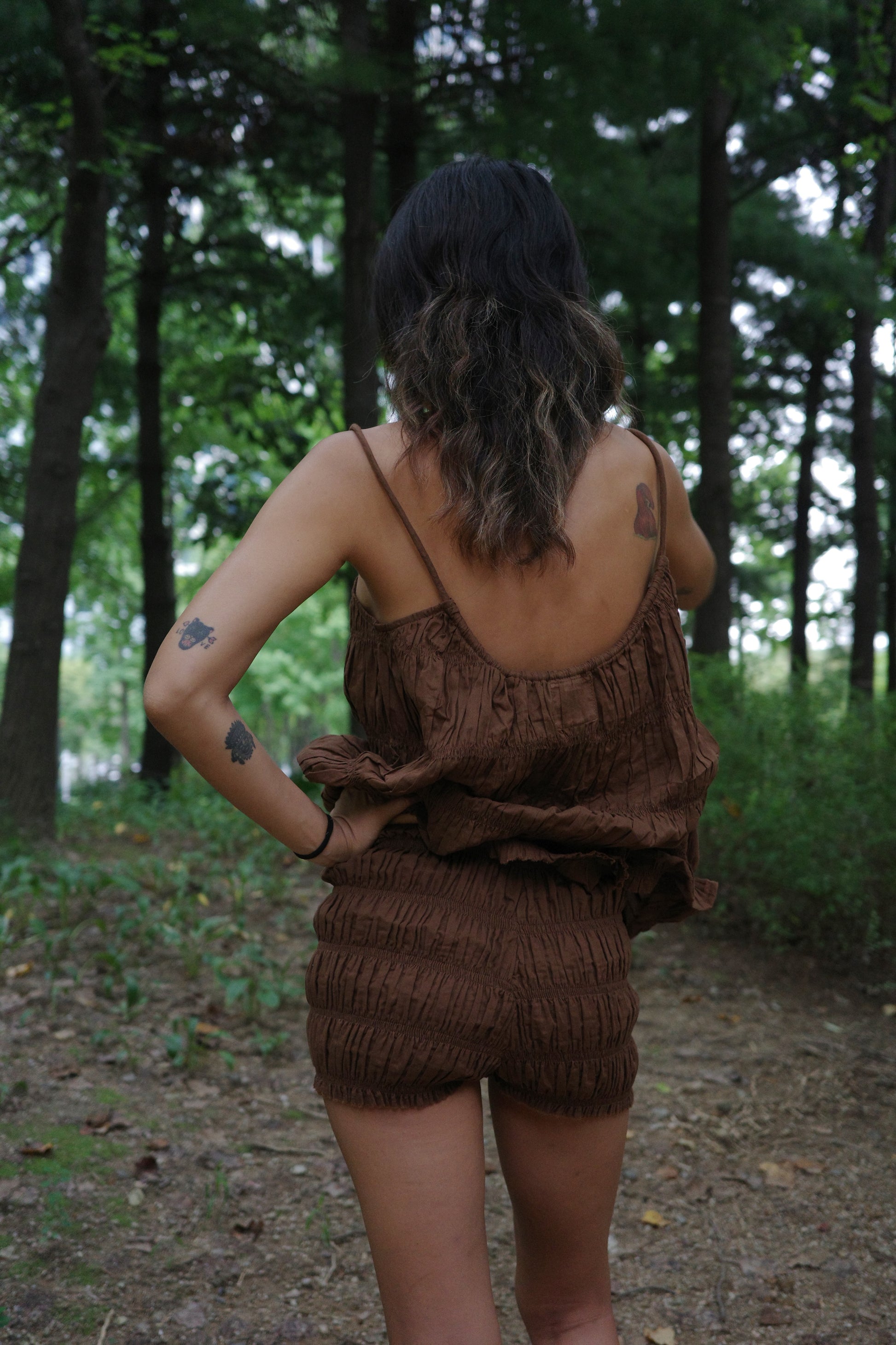 woman wearing a brown ruffle top and shorts in a forest setting