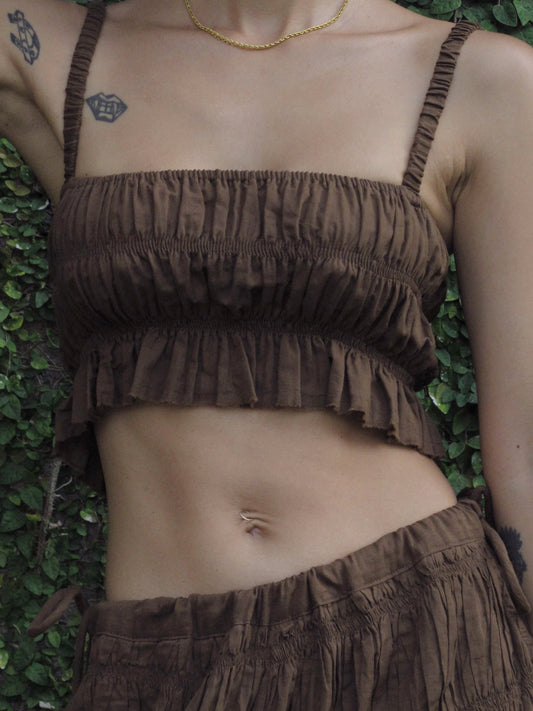 Person wearing a brown ruffled top  against a green leafy background