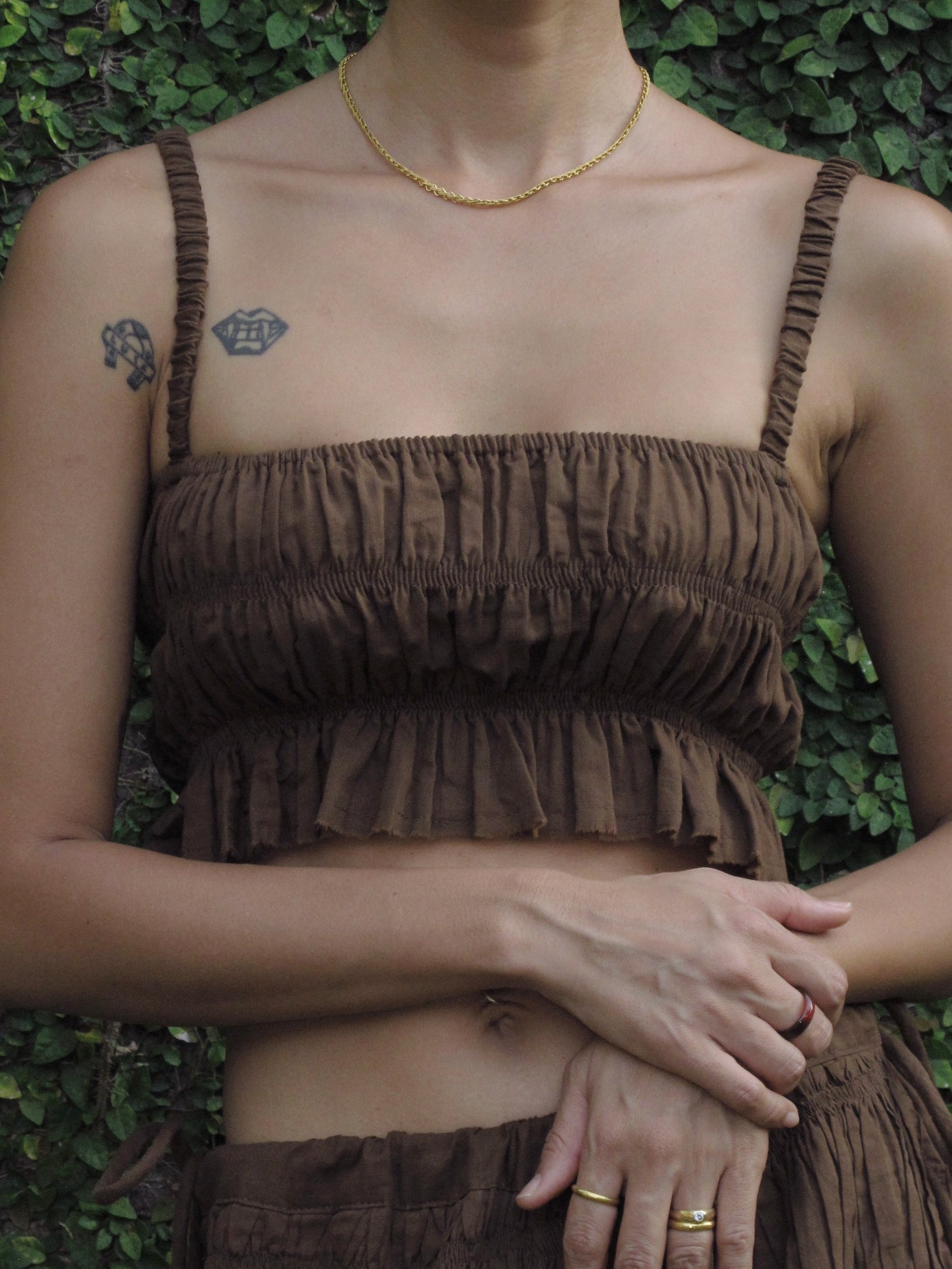 Person wearing a brown top with ruffled layers against a green leafy background