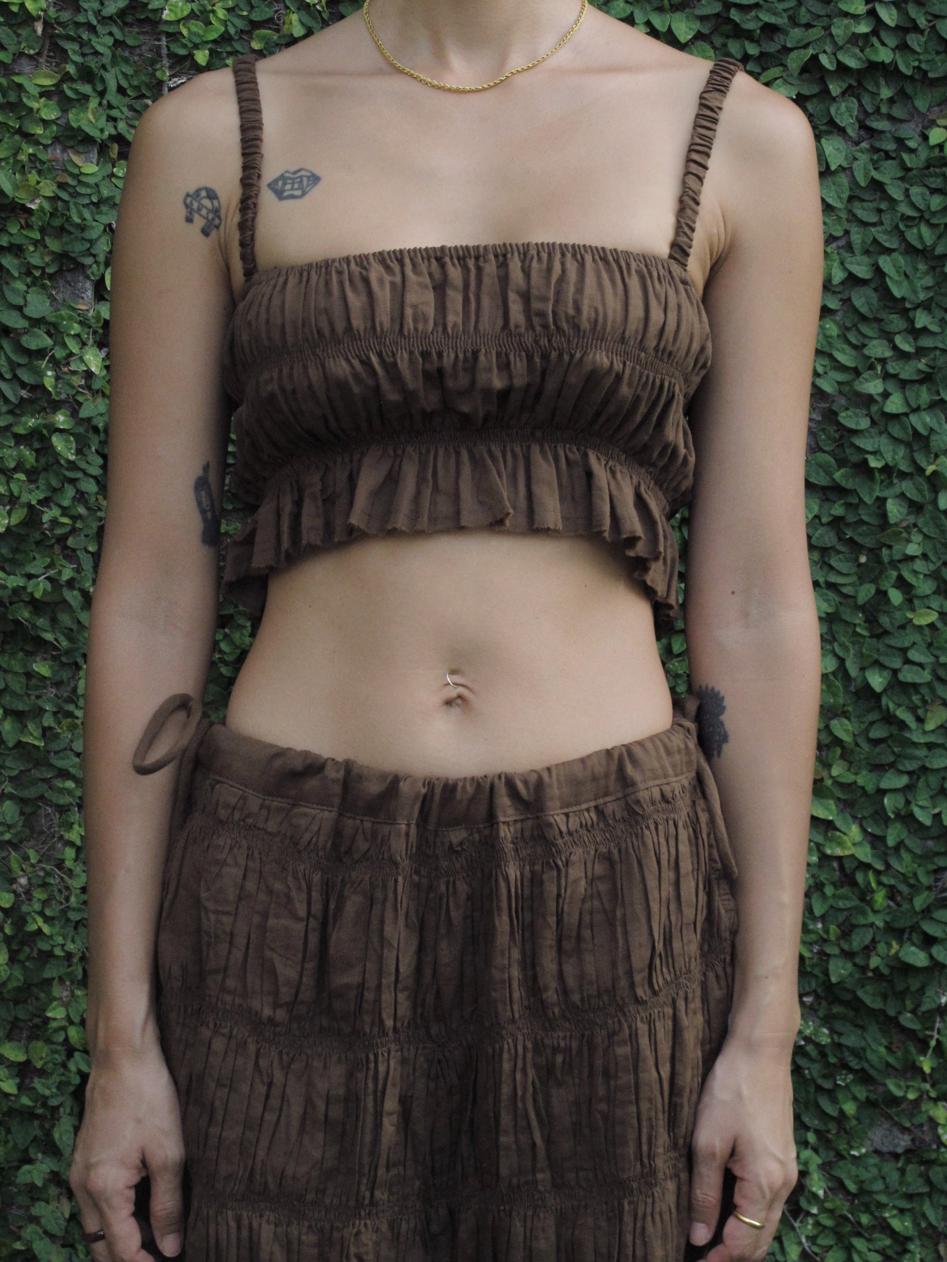 Person wearing a brown textured top and pants against a green leafy background