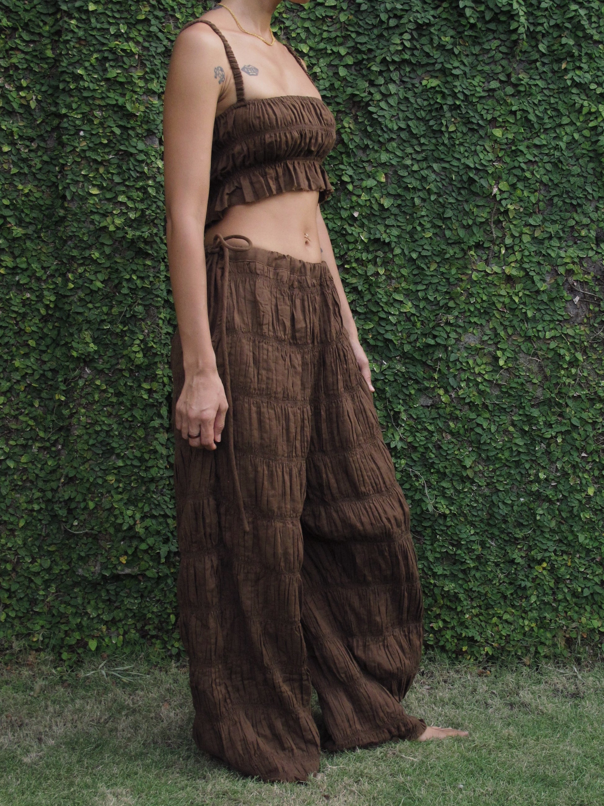 Person wearing a brown fringe outfit standing against a green hedge.