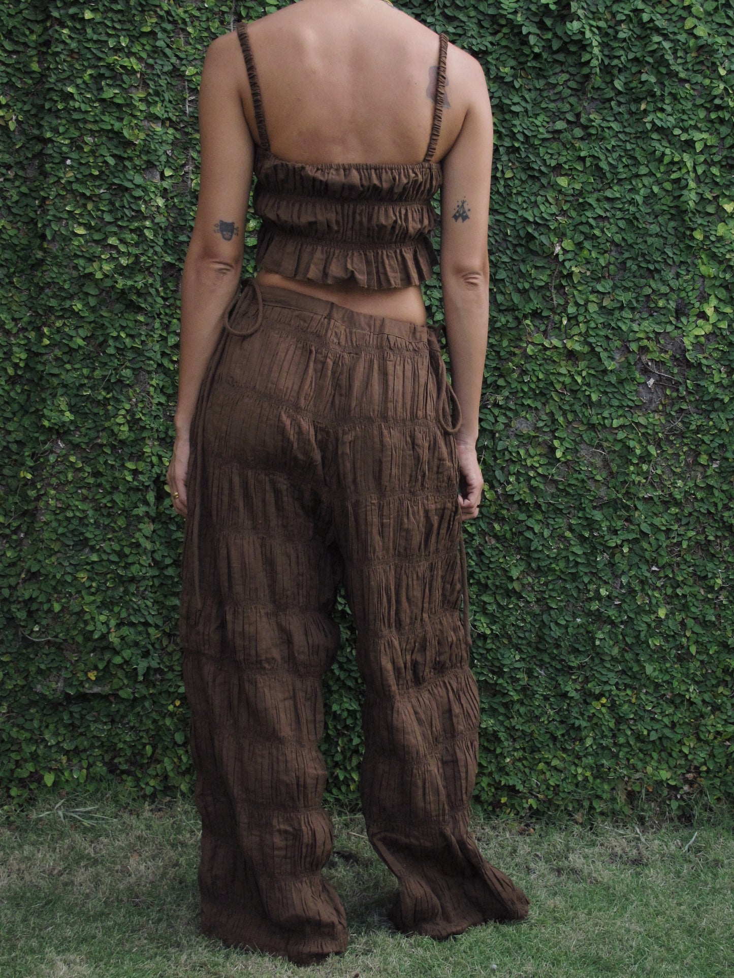 Person wearing a brown textured outfit standing against a green leafy background