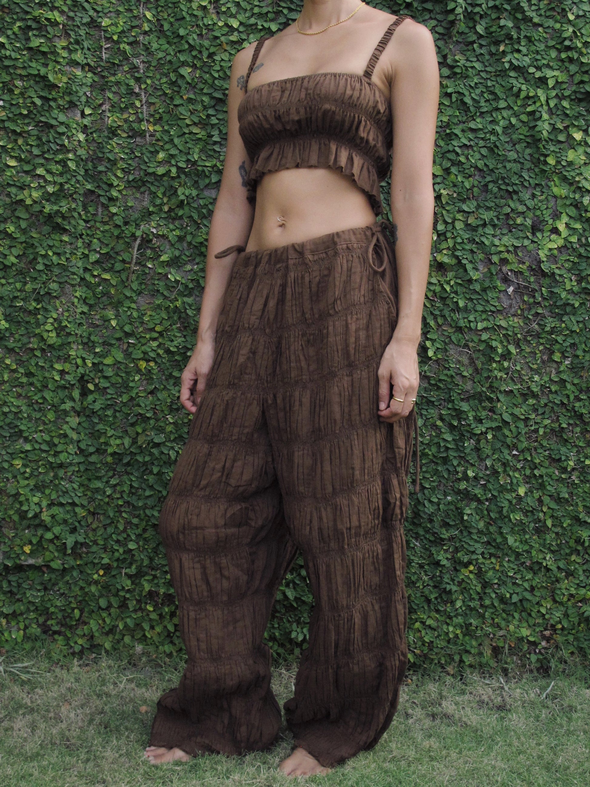 Person wearing a brown ruffled outfit standing against a green leafy background