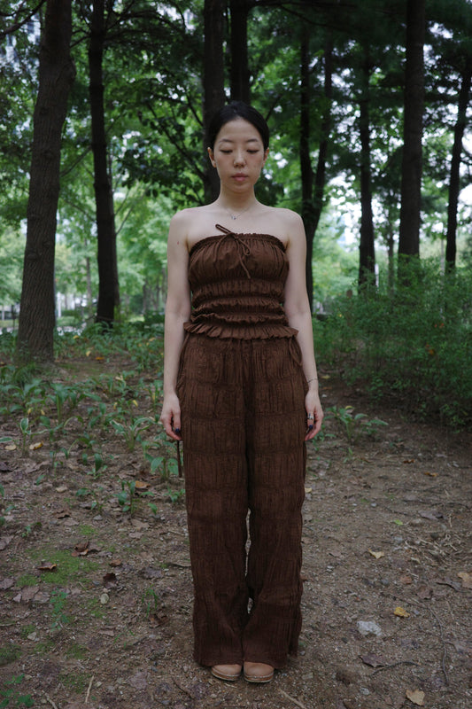 woman in a brown tube top and tie wide long pants standing in a forest