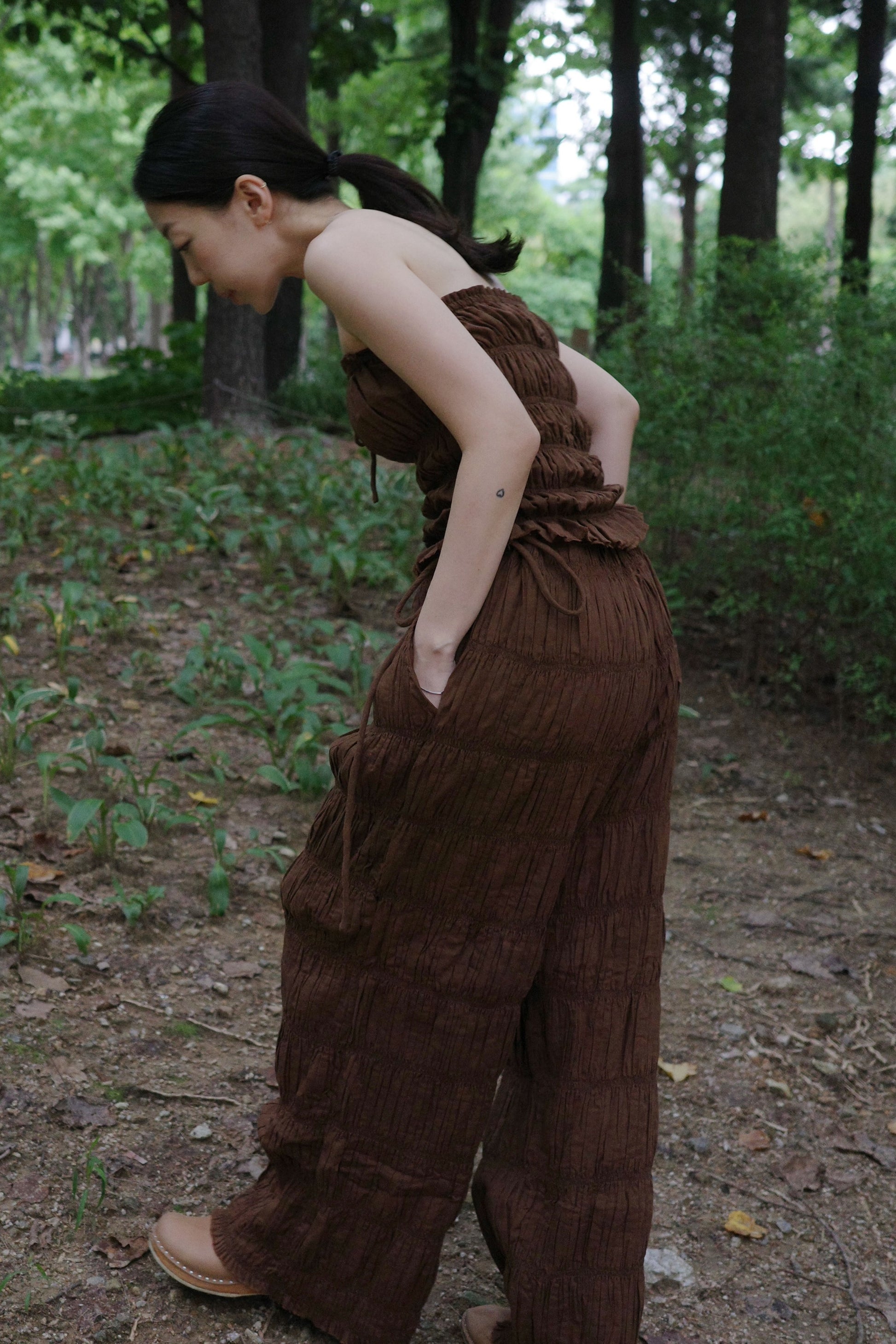 woman in a brown tube top and tie wide long pants standing in a forest
