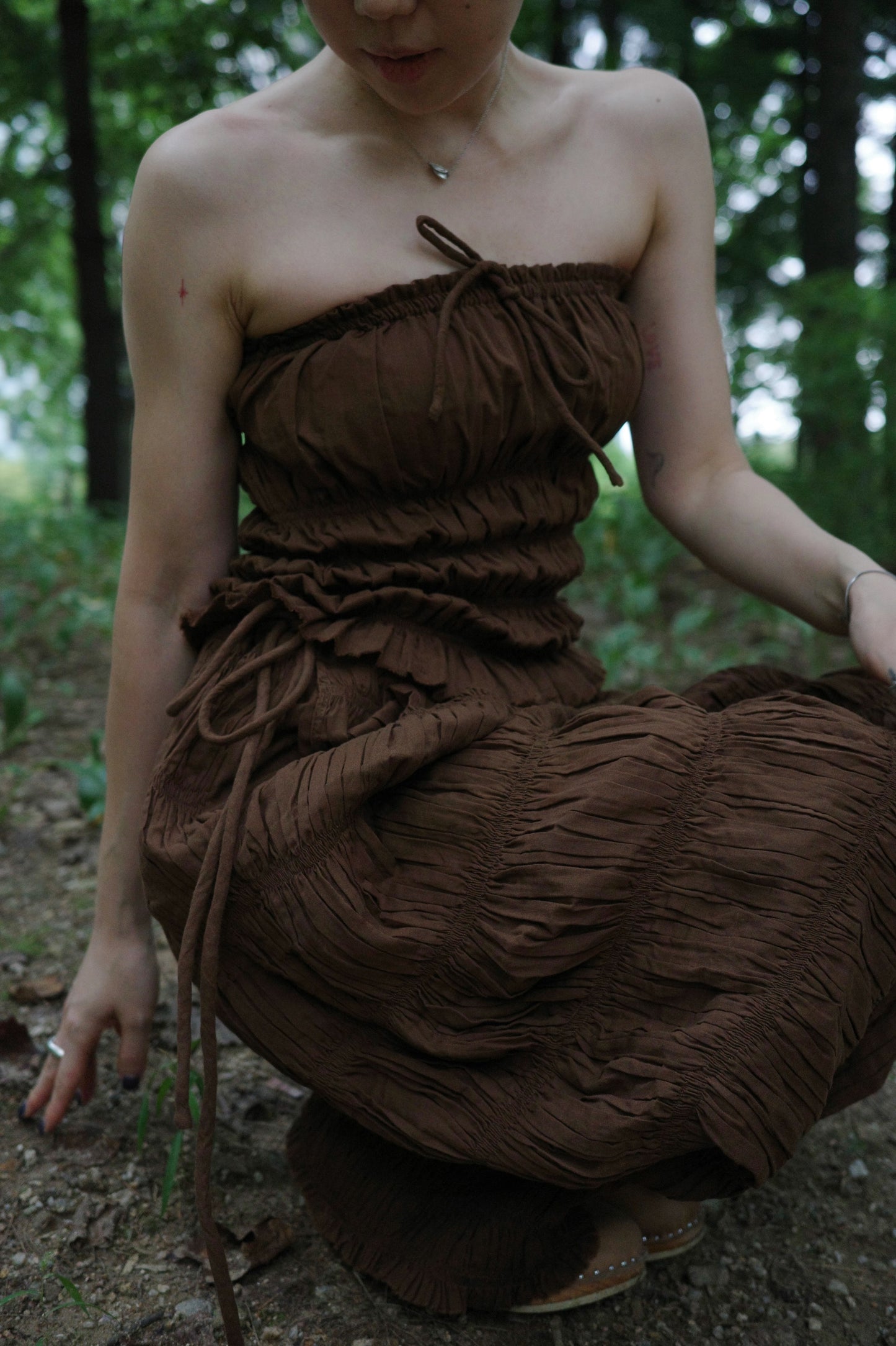 woman in a brown tube top and tie wide long pants sitting in a forest