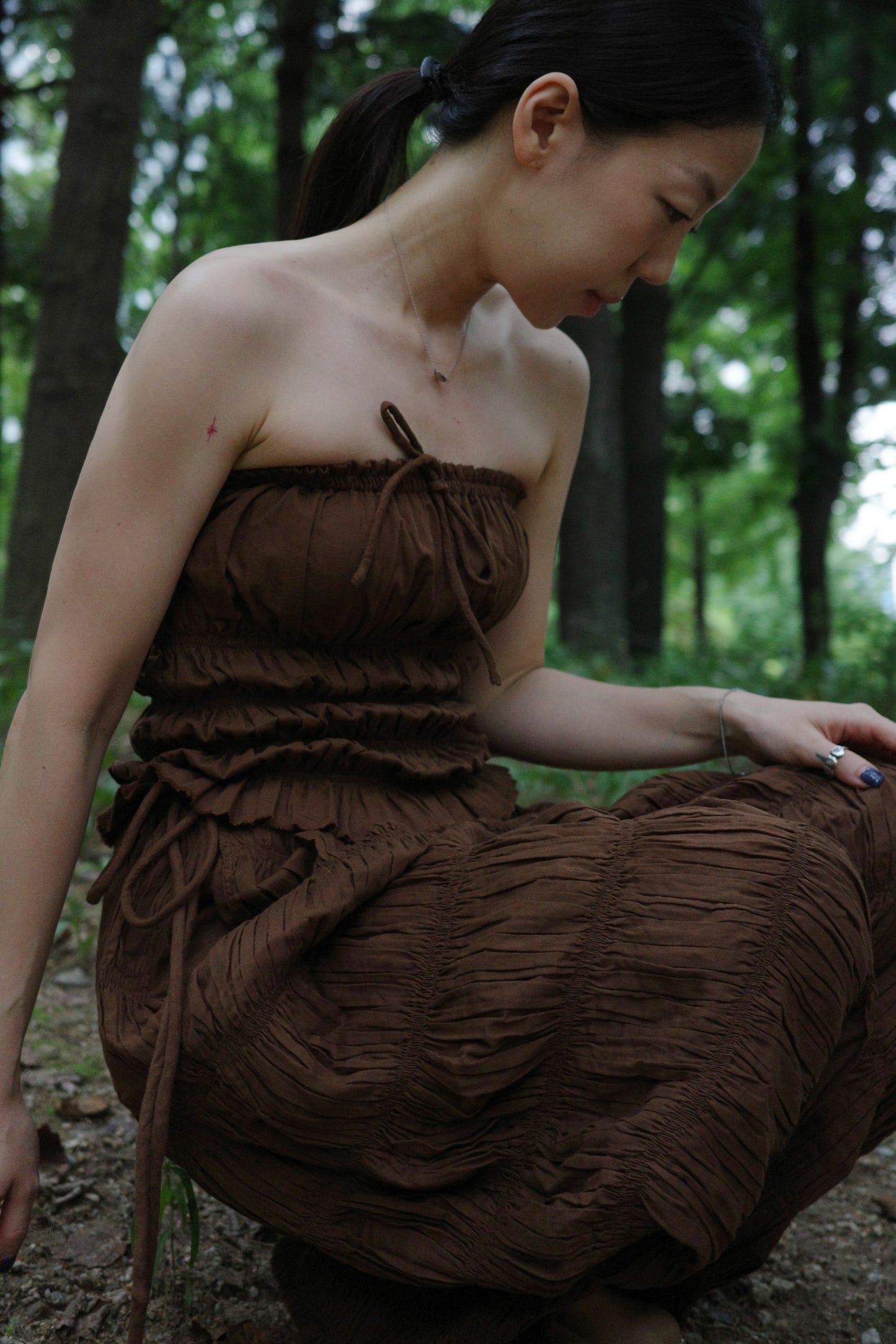 woman in a brown tube top and tie wide long pants sitting in a forest