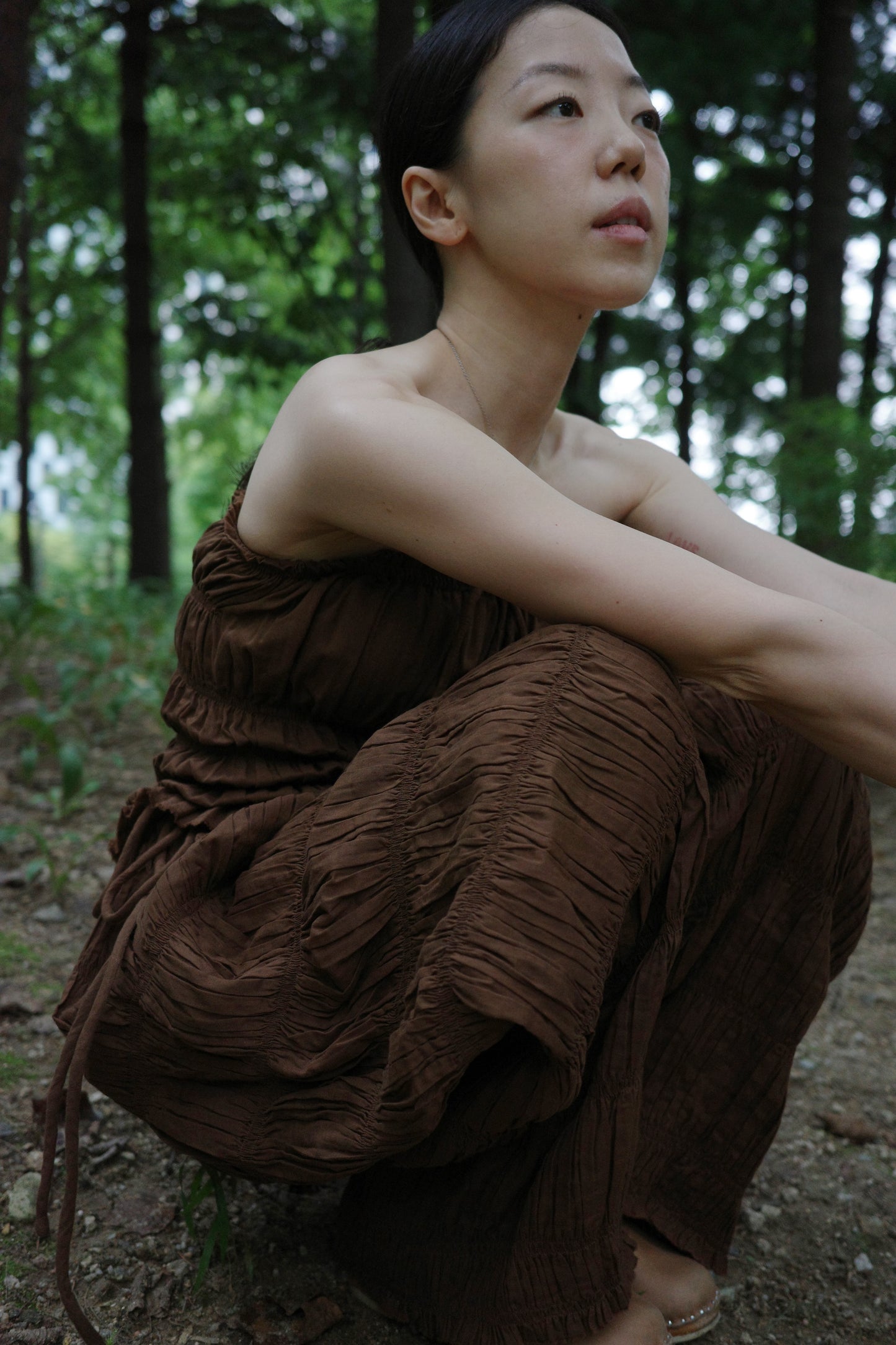 woman in a brown tube top and tie wide long pants sitting in a forest