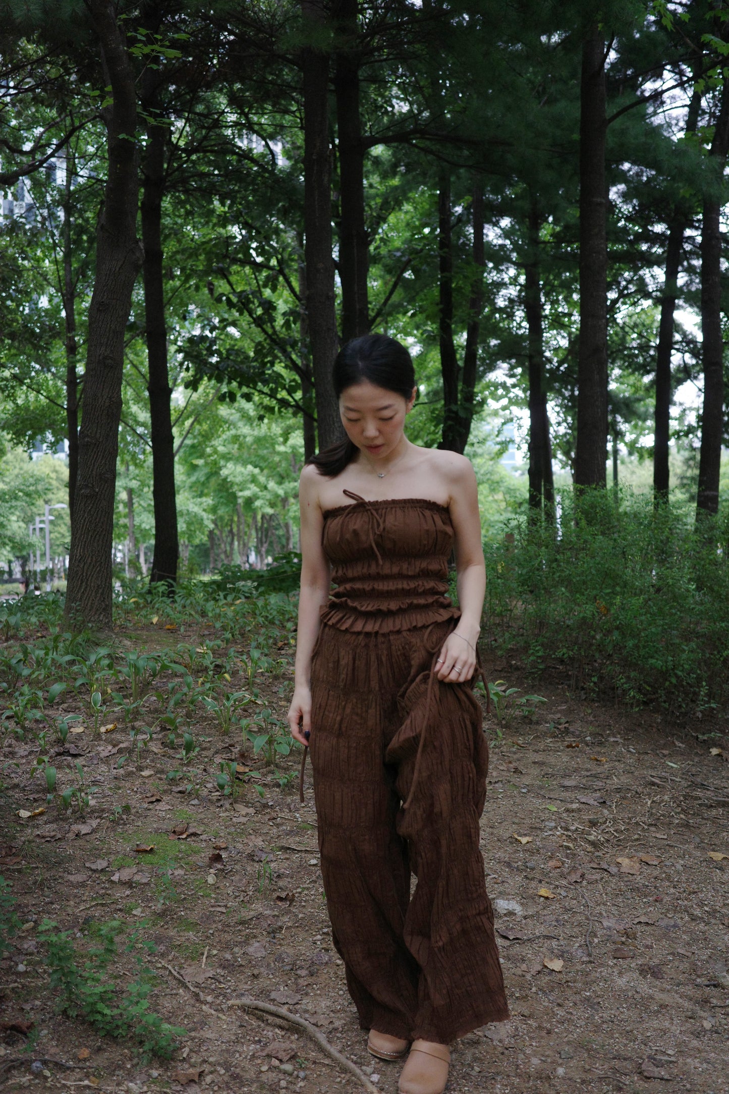 woman in a brown tube top and tie wide long pants walking in a forest