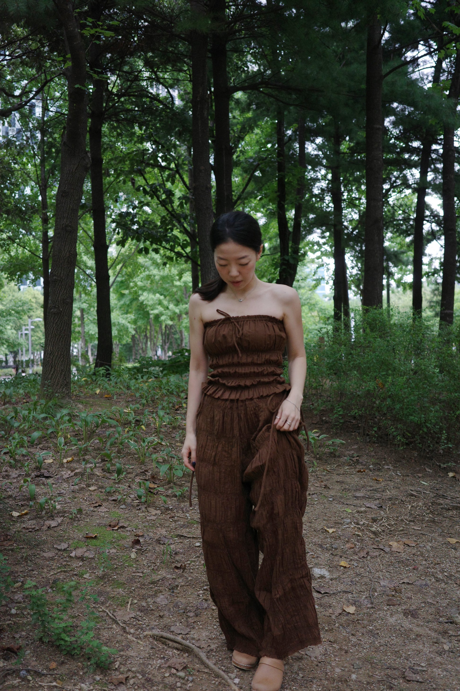 woman in a brown tube top and tie wide long pants walking in a forest