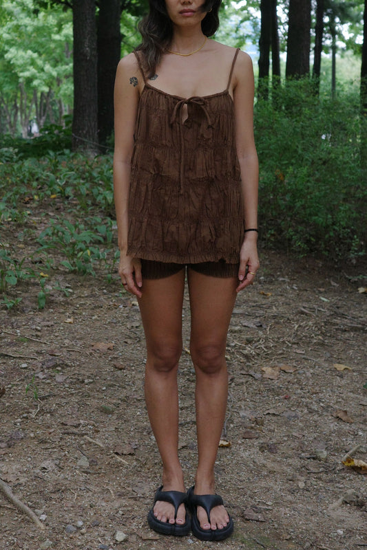 woman wearing a brown ruffled top and shorts standing in a forest setting