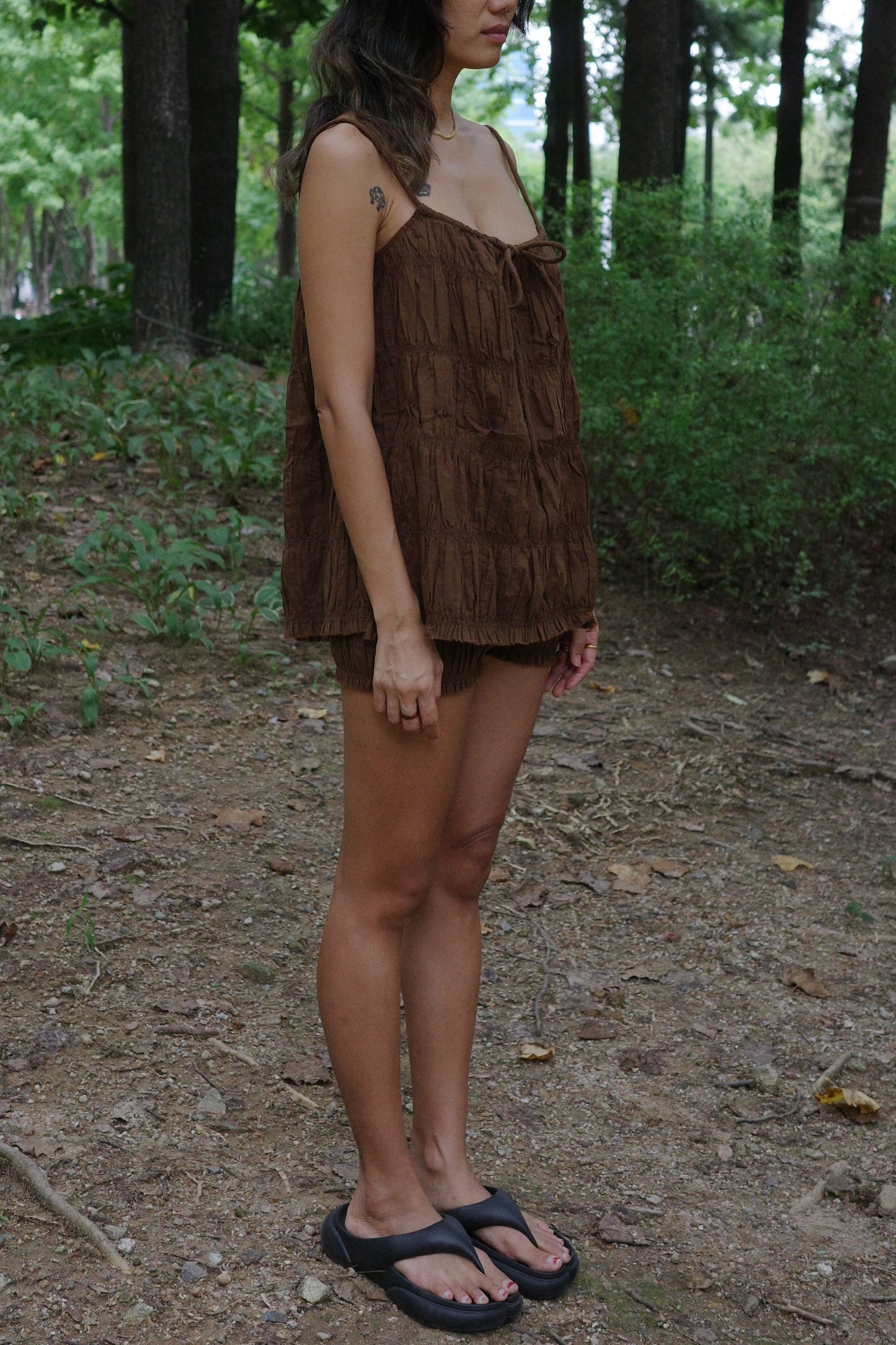 Woman in a brown ruffle top and shorts standing in a forest