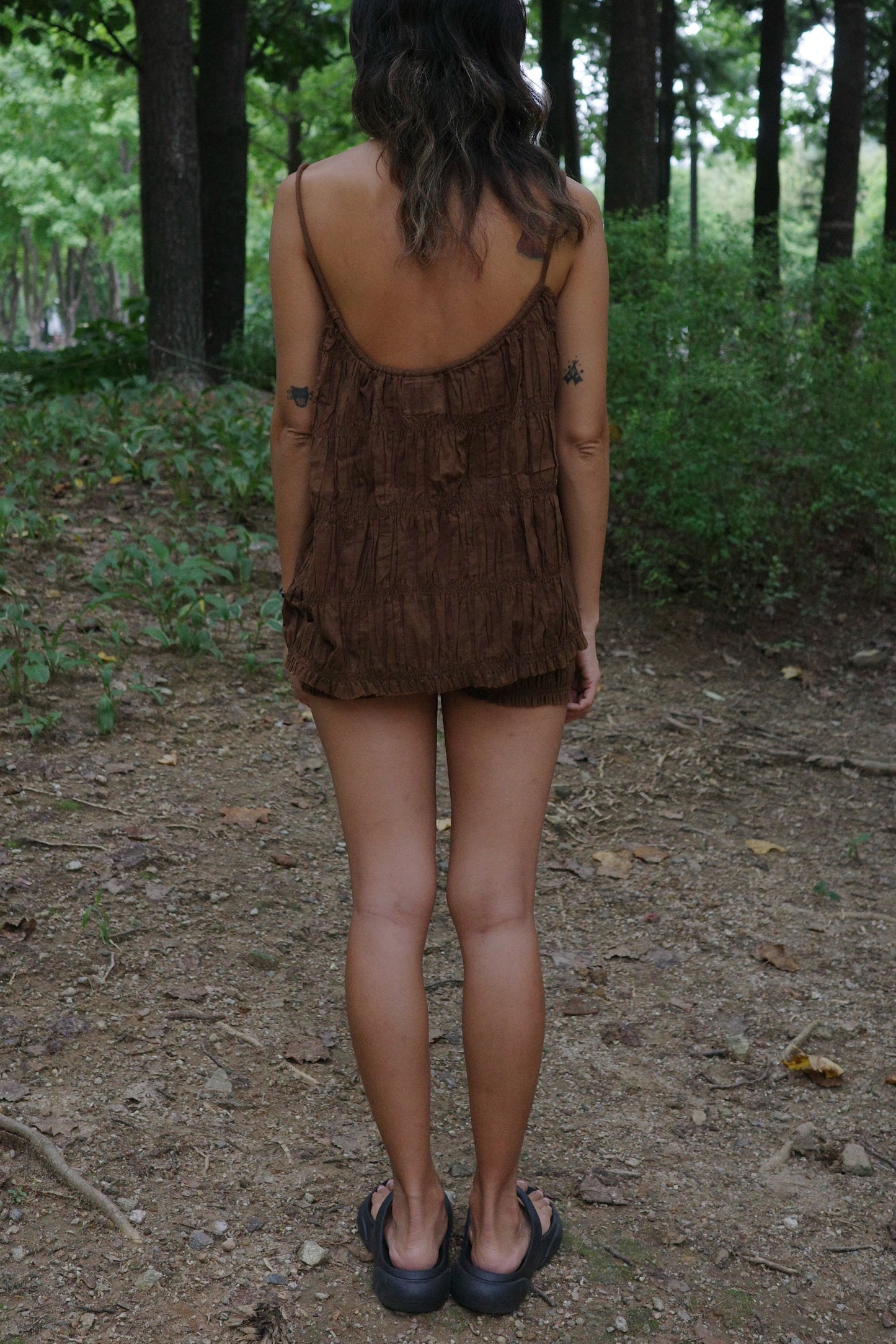 woman wearing a brown ruffle top and short standing in a forest
