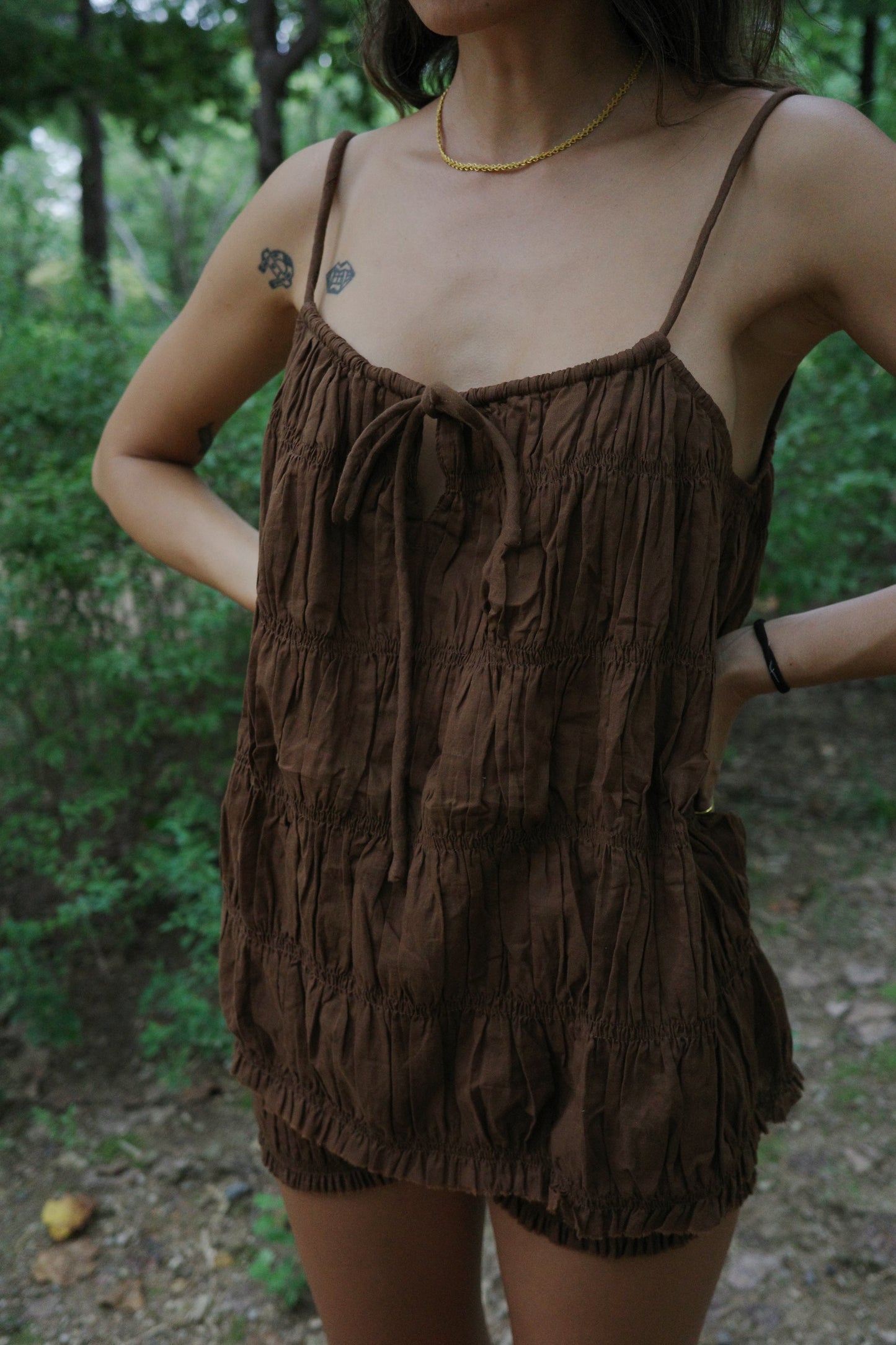 woman wearing a brown ruffle string top  in a forest setting