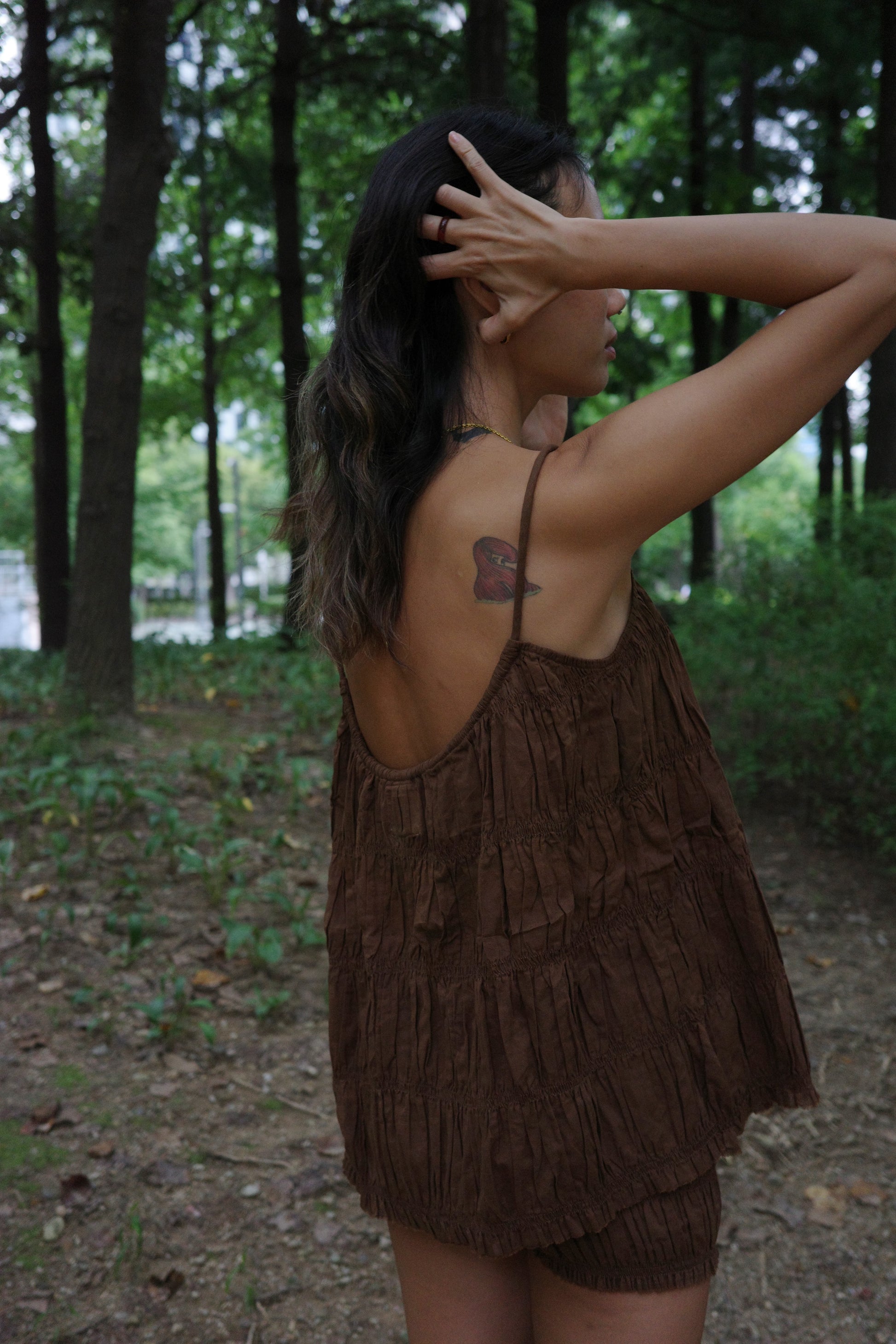 Woman in a brown ruffle string top standing in a forested area