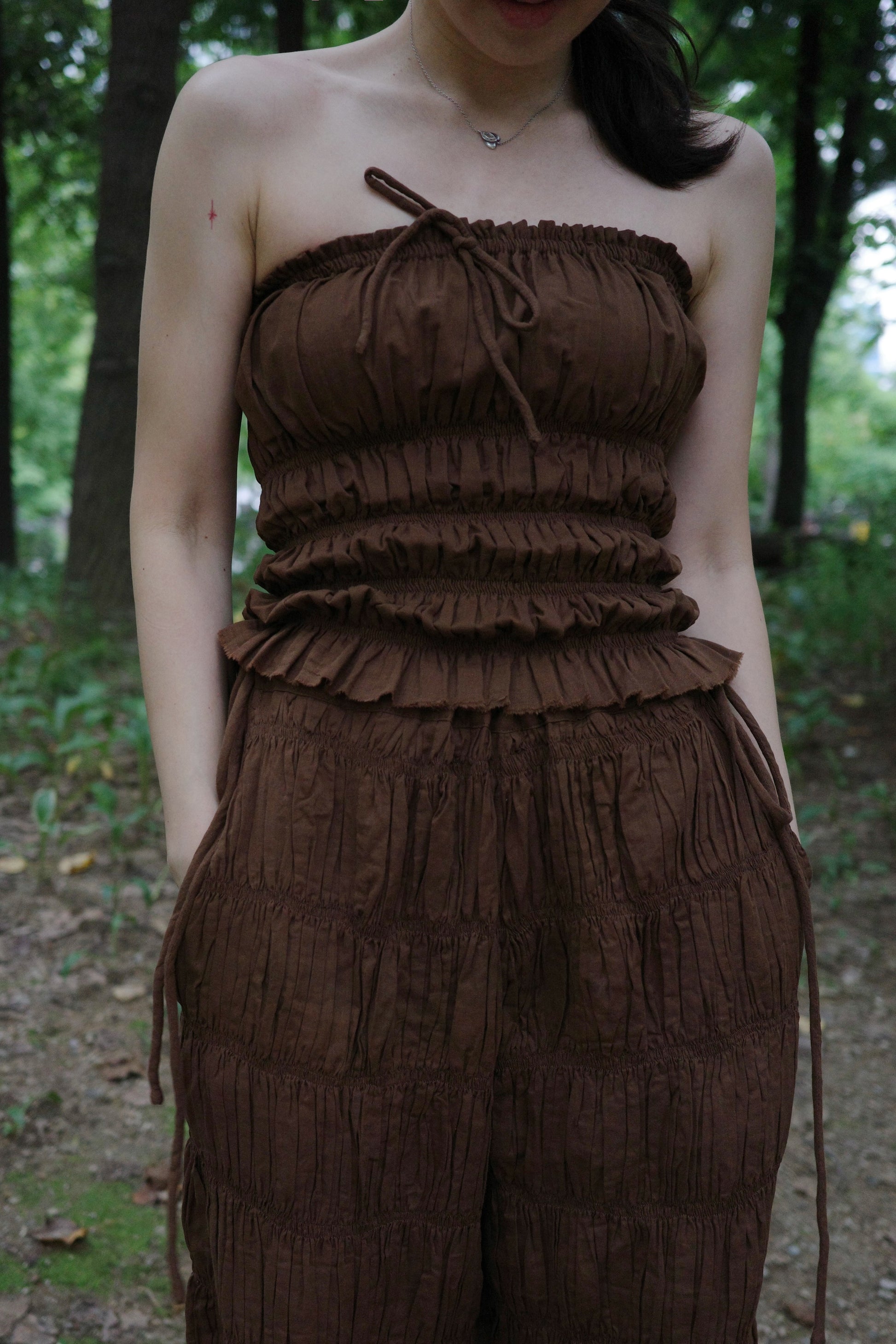 woman wearing in a brown tube top  standing in a forest 