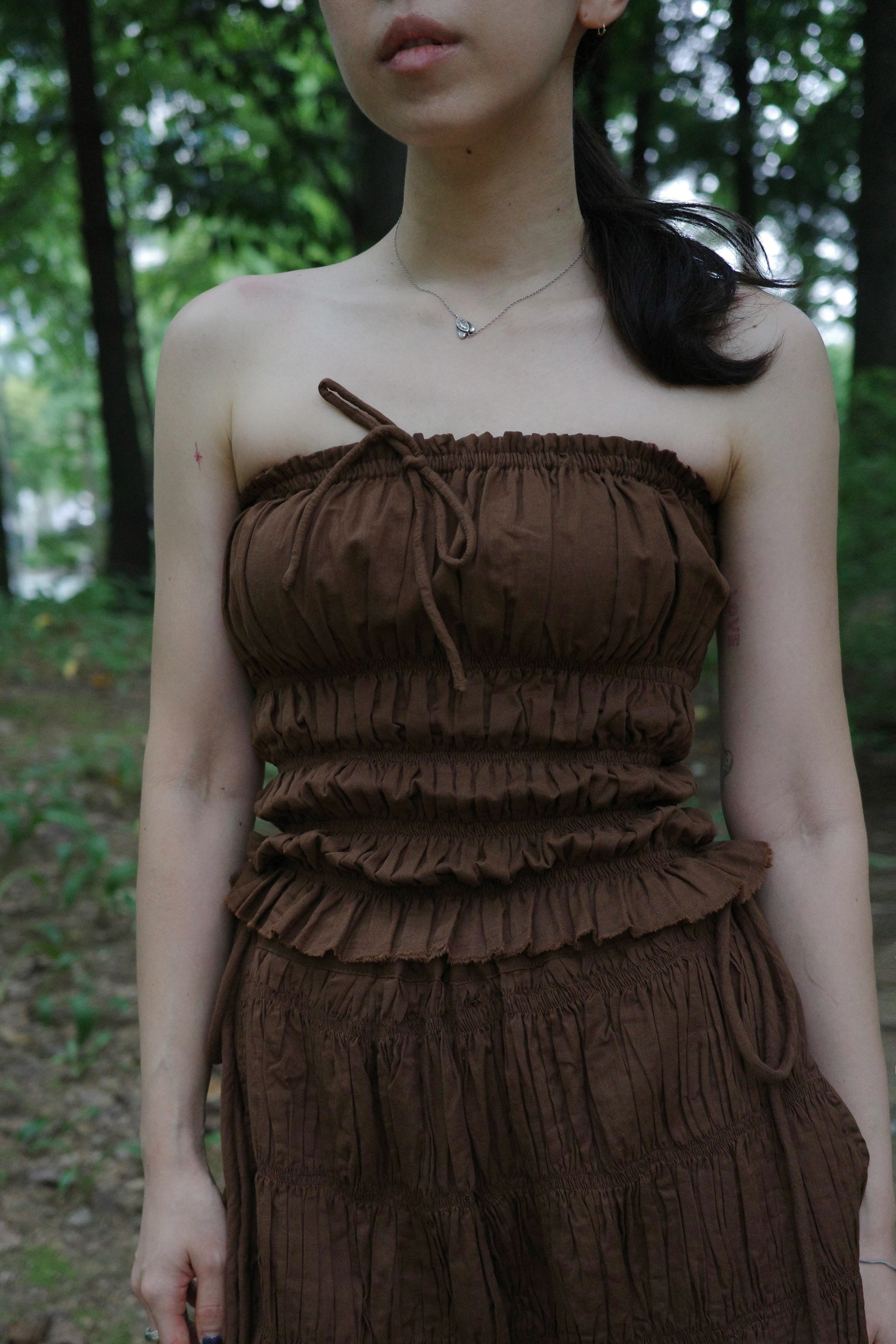 woman wearing in a brown tube top standing in a forest 
