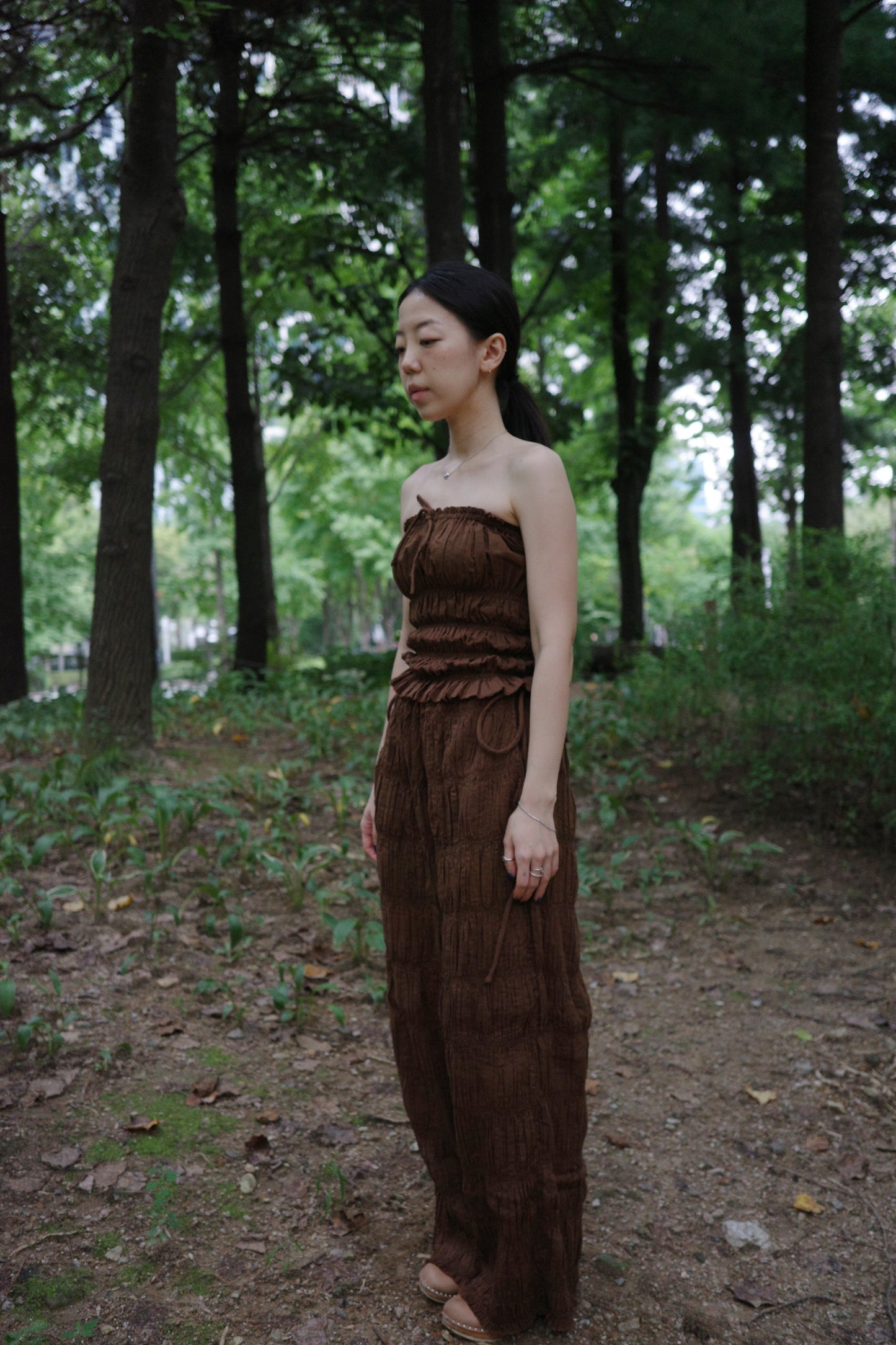 woman wearing in a brown tube top standing side profile in a forest 