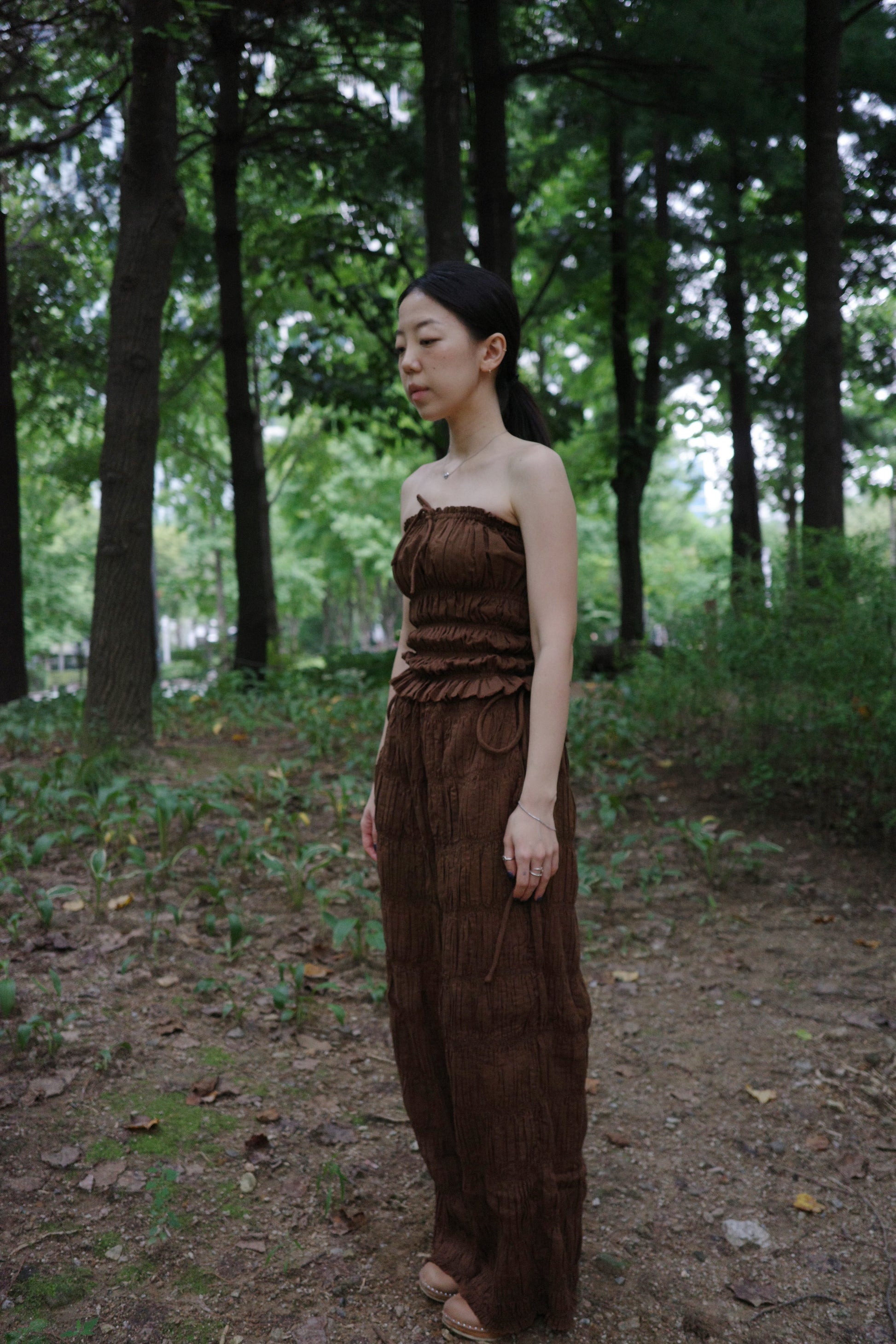 woman wearing in a brown tube top standing side profile in a forest 