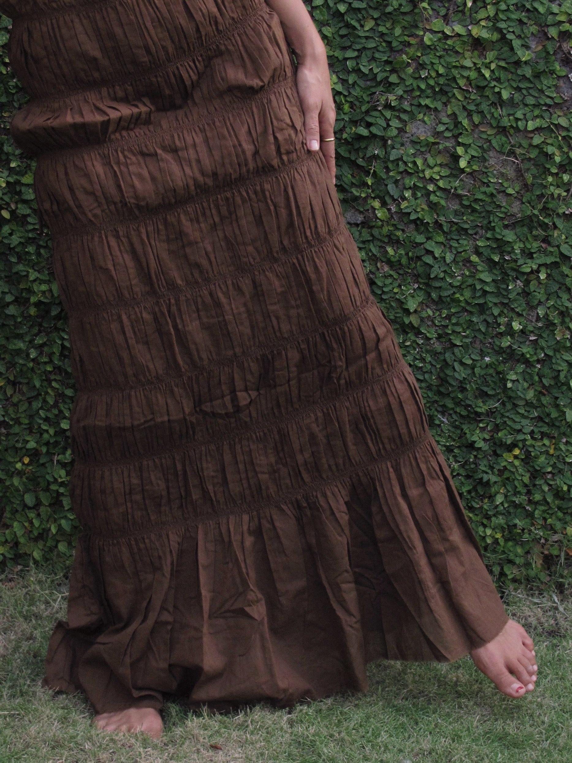 Brown cocktail dress worn by a person against a green leafy background