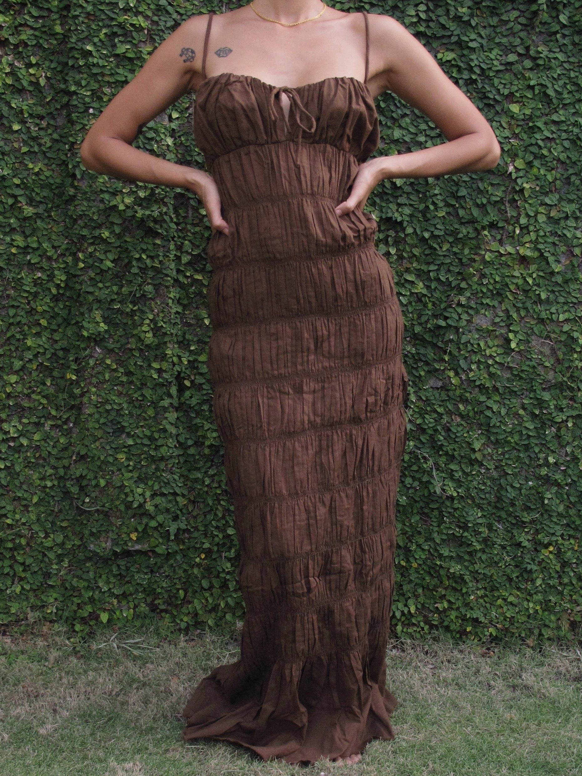 Woman wearing a brown ruffle dress against a green hedge backgroun