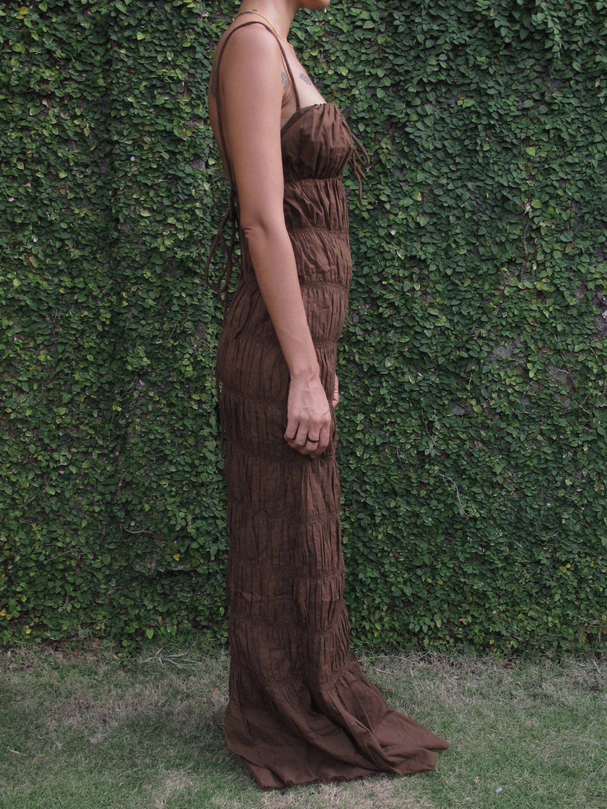 Person wearing a brown cocktail dress against a green hedge background