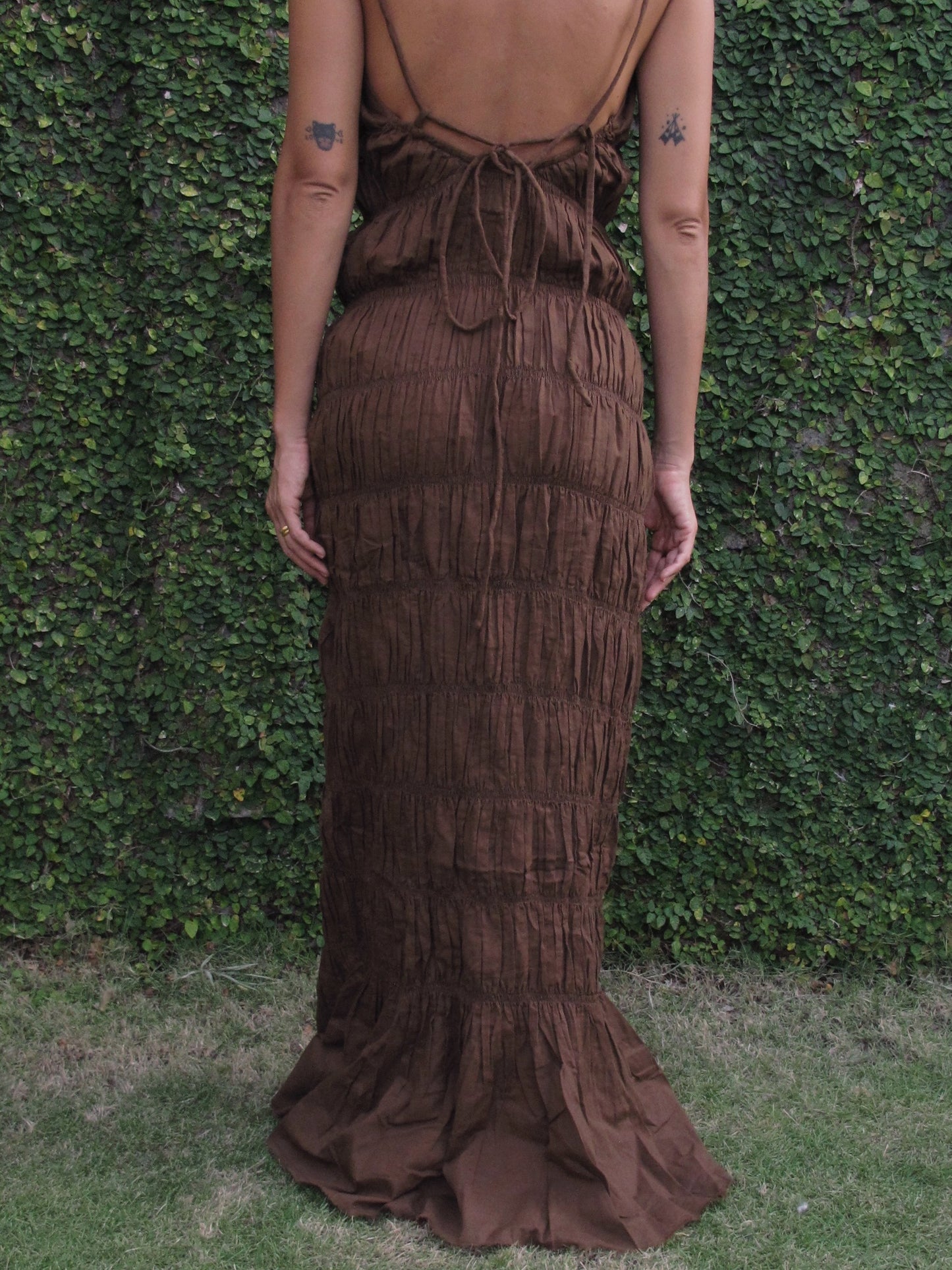Brown tiered dress worn by a person against a green hedge background
