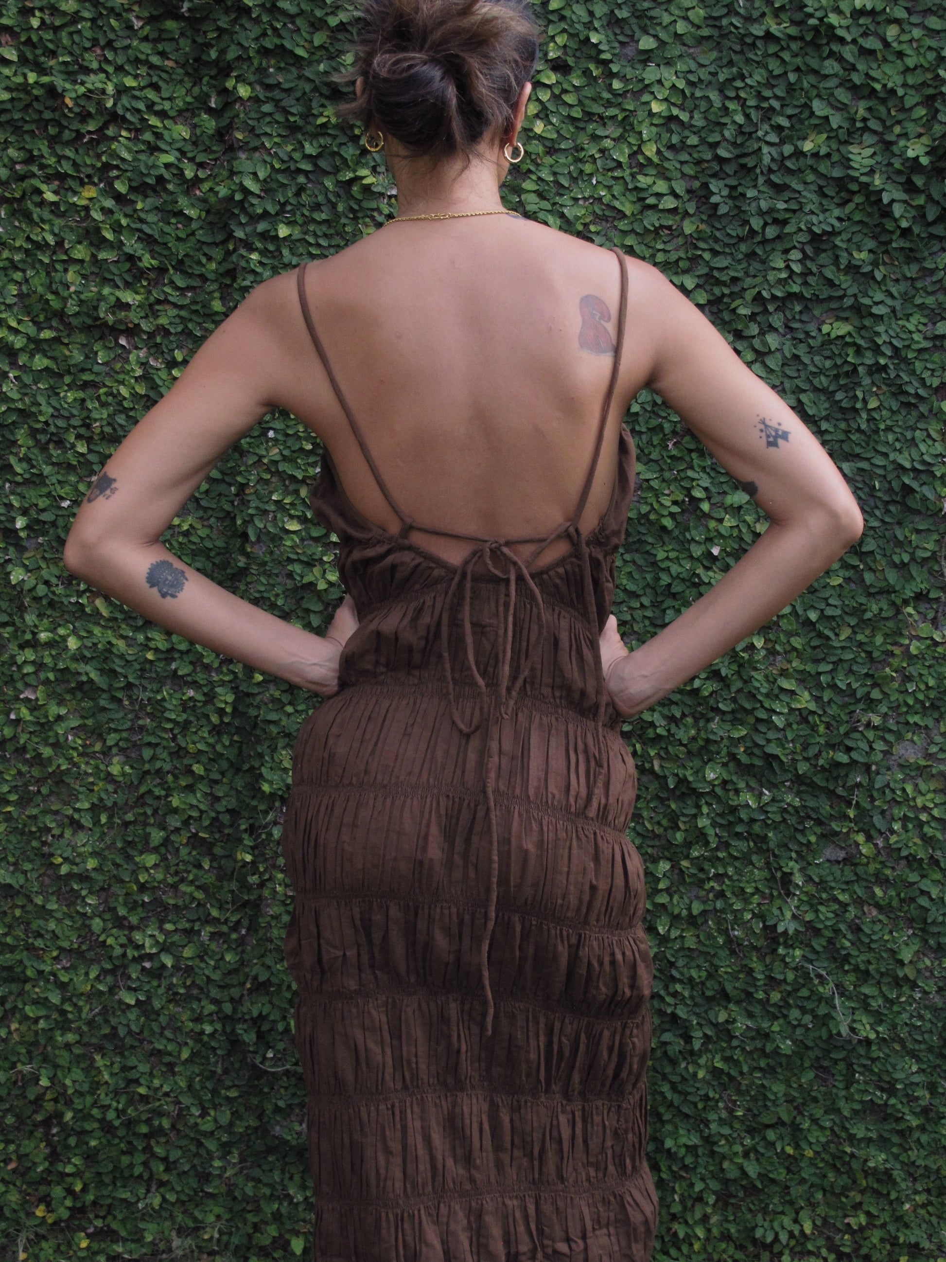 Person wearing a brown dress with a textured pattern against a green leafy background