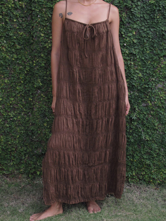 Person wearing a brown tiered dress against a green hedge background