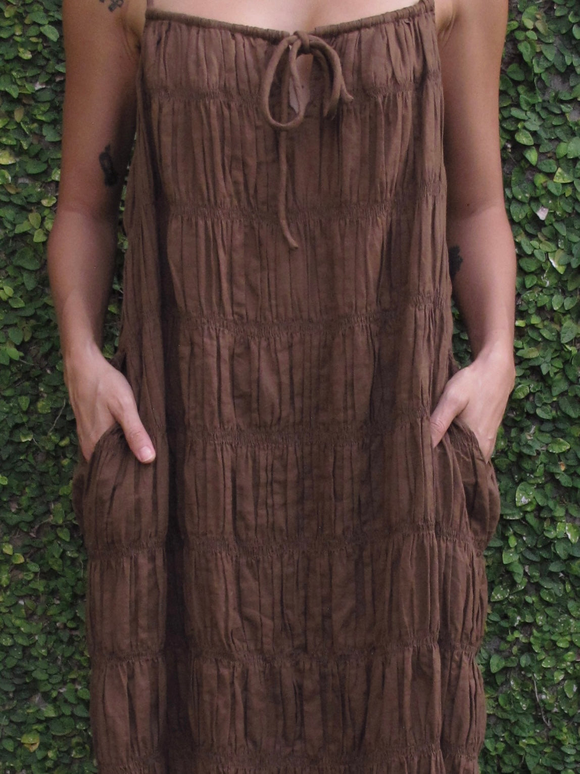 Brown strapless dress worn by a person against a green leafy background