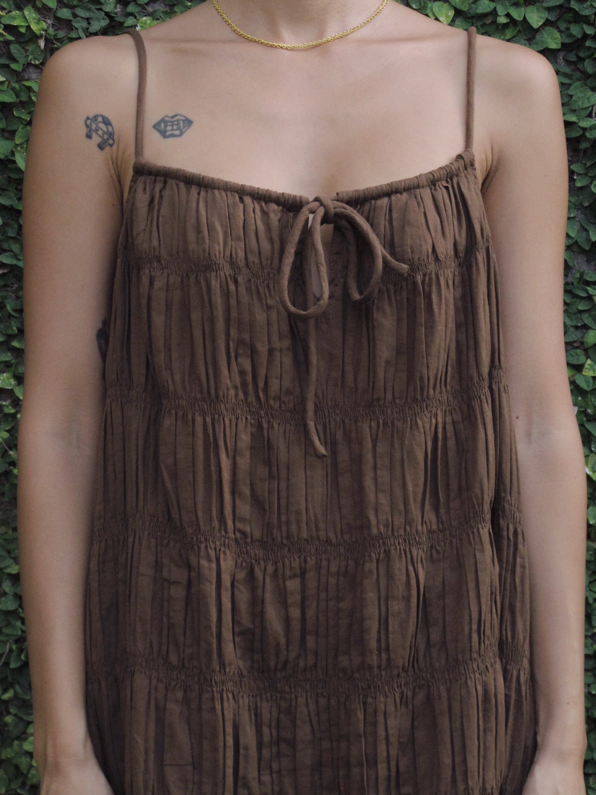 Brown textured dress worn by a person against a green leafy background