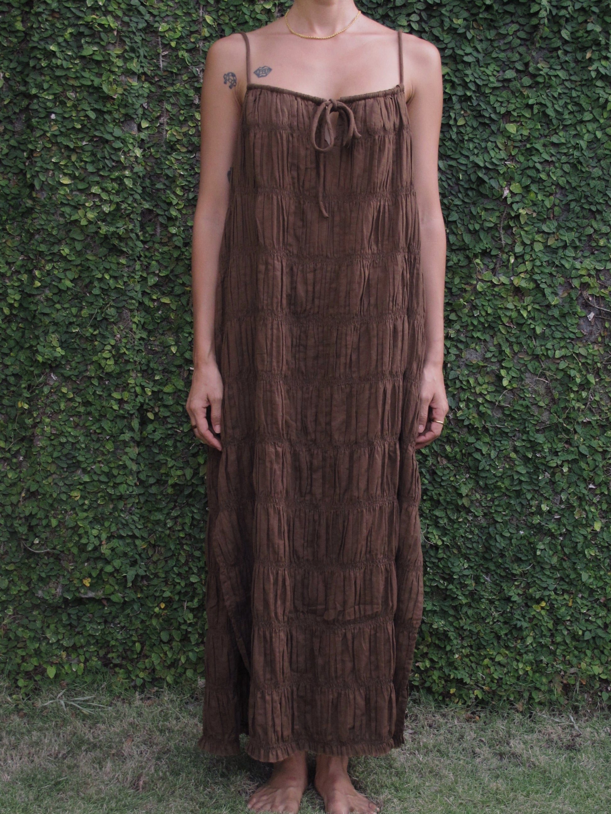Person wearing a brown fringe dress standing against a green leafy background