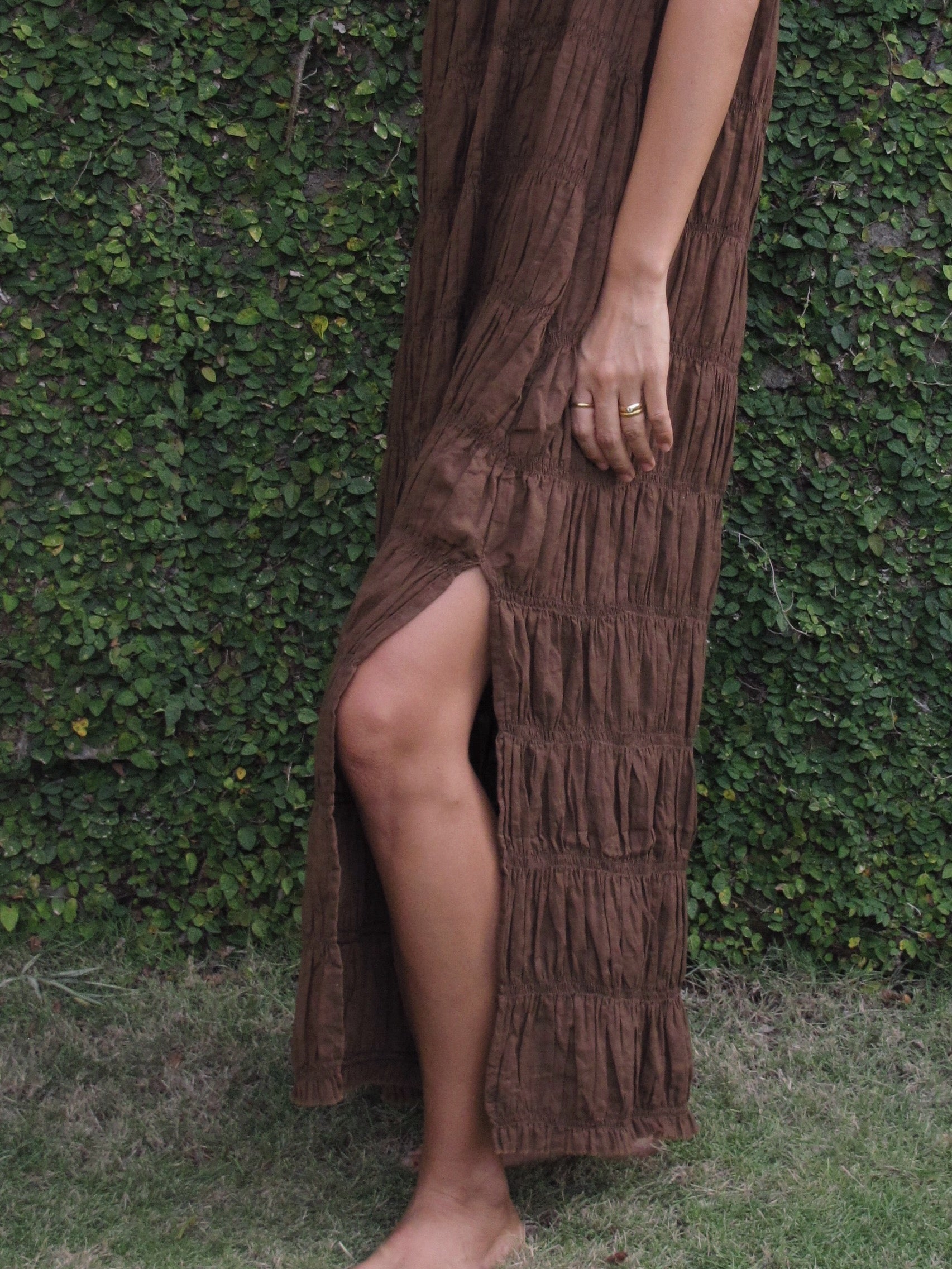 Brown textured dress with a slit worn by a person against a green leafy background